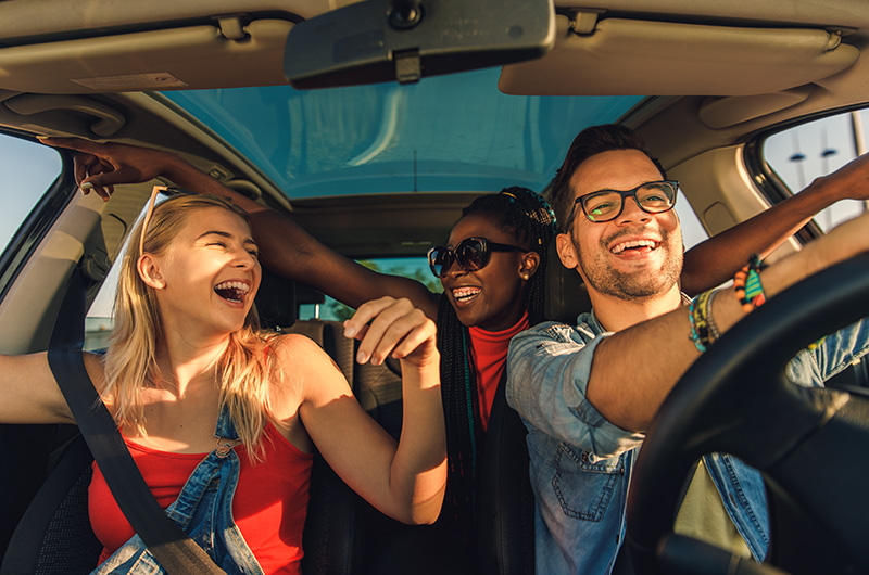 friends-listening-to-audio-system-car Three friends laughing and enjoying music together while driving in a car.