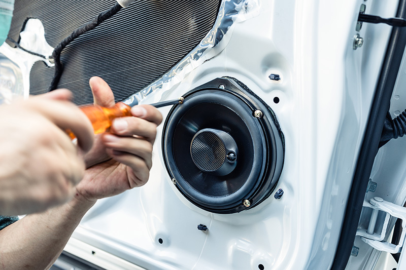 installing-new-audio-system Technician installing a car door speaker using a screwdriver.