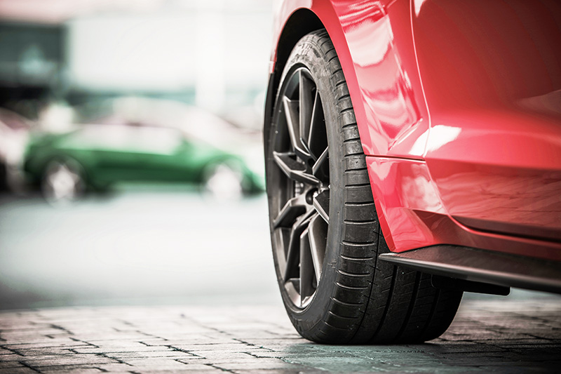 sports-car-wheel-closeup Close-up of a red sports car wheel and tire with black alloy rim parked on a city street.